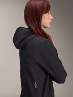 Alpinestars Stella A-Dura Thermojacke, Damen-Fahrradjacke, Schwarz, Seitenprofil einer Frau mit roten Haaren, die die Jacke trägt, verfügt über eine integrierte Kapuze und ein weißes Alpinestars Stern-Logo an der Seite, leichte isolierte Thermo-Ausrüstung für MTB.