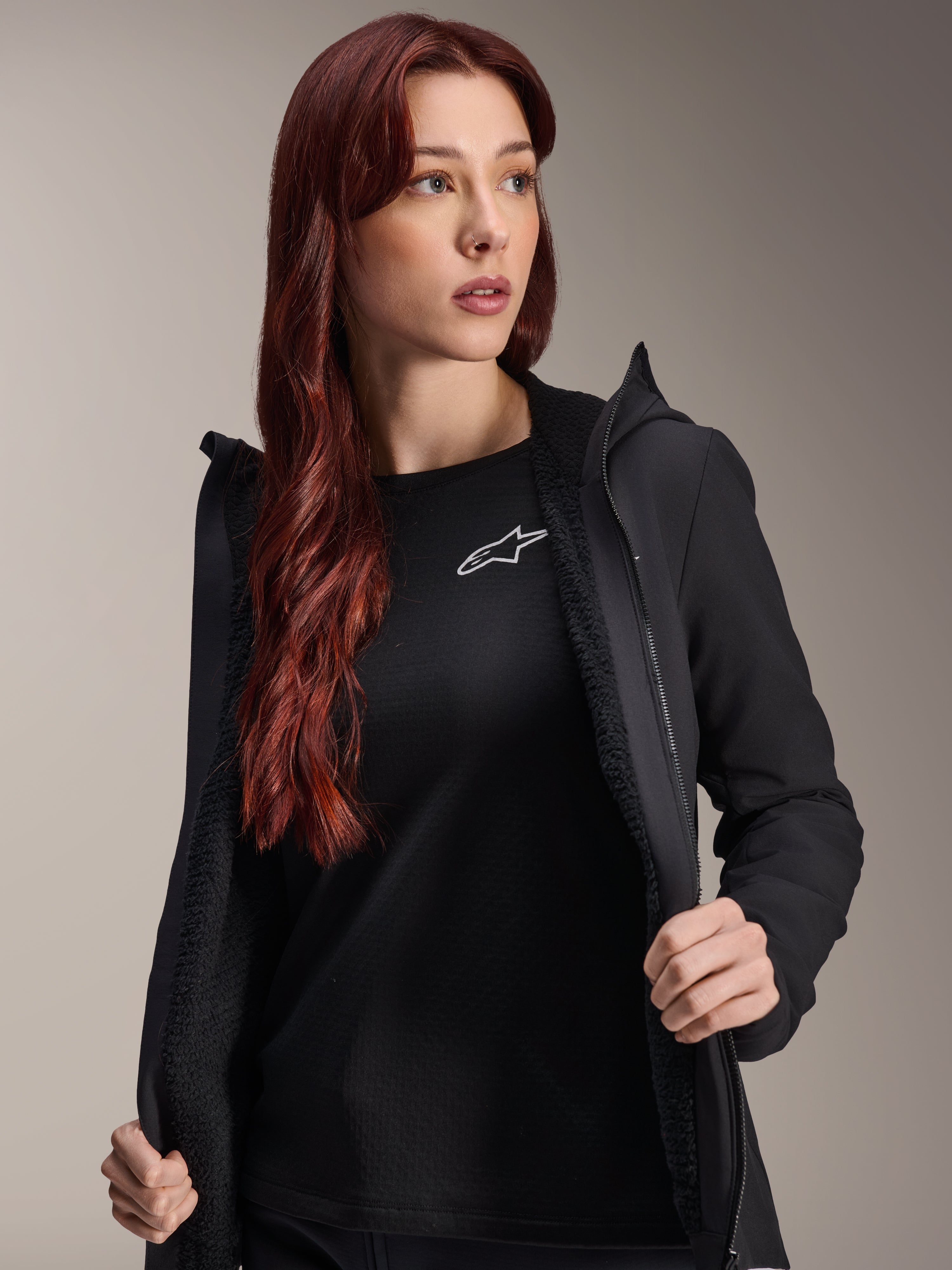 Alpinestars Stella A-Dura Thermojacke, schwarze Radjacke für Damen, offen getragen mit strukturiertem Fleece-Futter und Frontreißverschluss, über einem schwarzen T-Shirt mit Alpinestars-Logo, leicht und isoliert für Fahrten bei kaltem Wetter