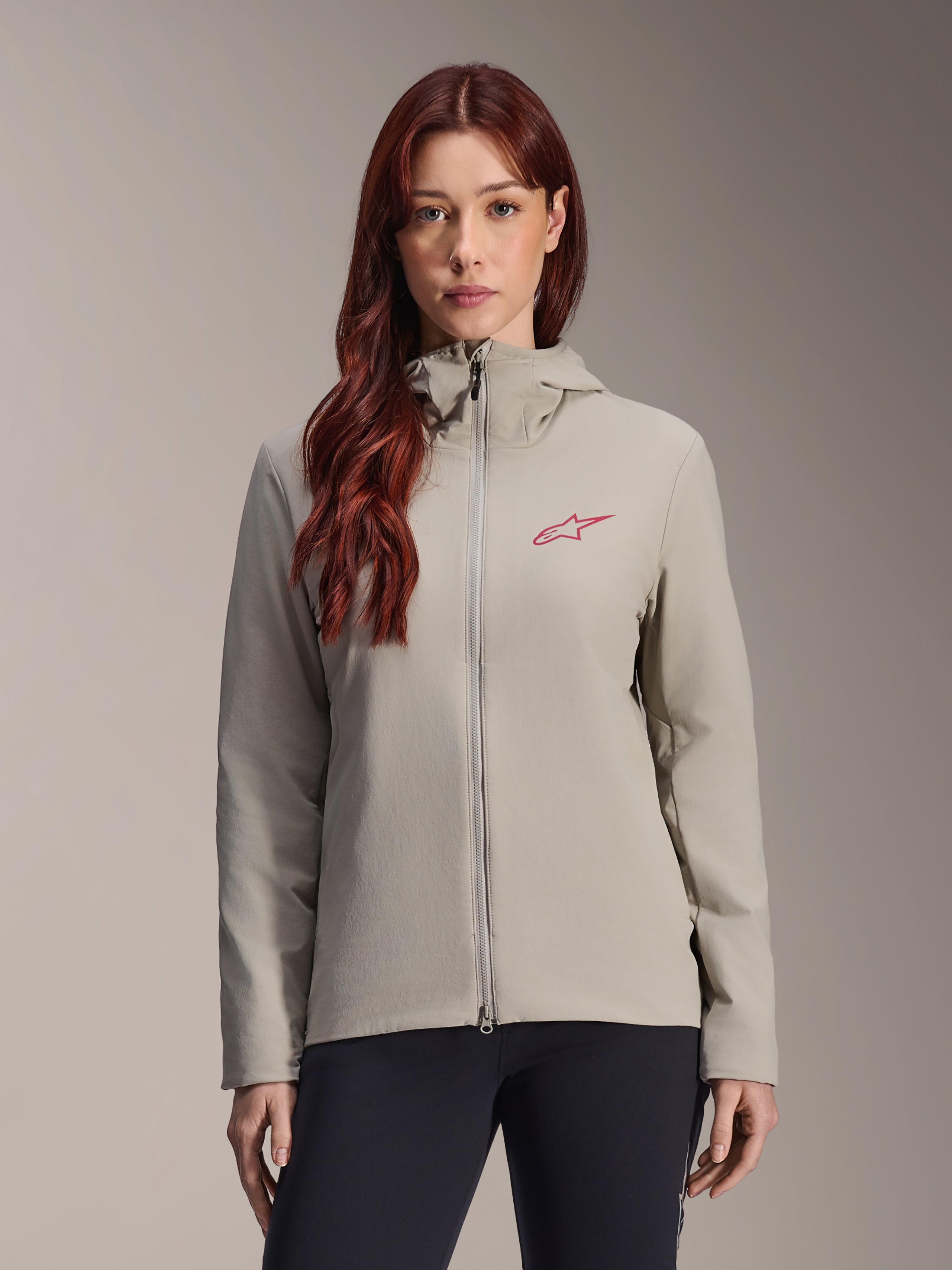 Alpinestars Stella A-Dura Thermal Jacke für Damen, Titanium-Grau, Design mit Kapuze und Reißverschluss, rotes Stern-Logo auf der Brust, kombiniert mit schwarzer Hose, Lifestyle-Studio-Porträt