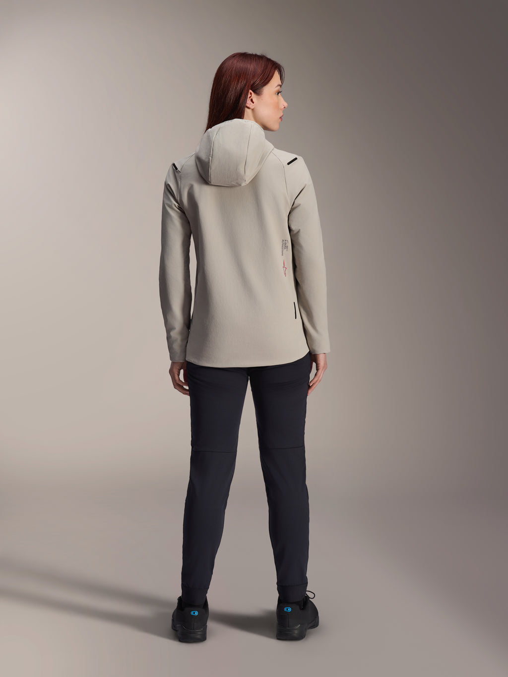 Alpinestars Stella A-Dura Thermal Damenjacke, Titanium Grau, Rückansicht getragen mit schwarzer Hose, mit fleecegefütterter, isolierter Kapuze und kleinem rotem Logo, funktionale und stylische Mountainbike-Jacke für Fahrten bei kaltem Wetter.