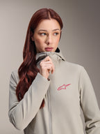 Alpinestars Stella A-Dura Thermojacke für Damen, Titanium-Grau mit pinkfarbenem Alpinestars Stern-Logo, Modell mit langem rotem Haar trägt die Kapuzenjacke und schließt den Reißverschluss, leichte isolierte Radbekleidung für kaltes Wetter