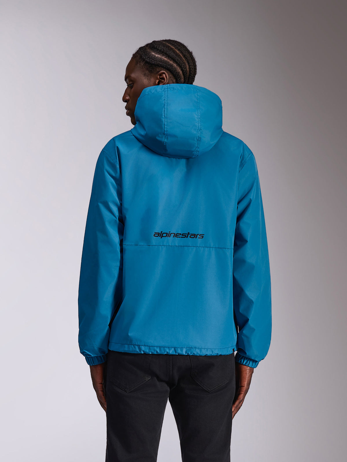Alpinestars Speeder Chromium Windbreaker-Jacke, Blau, Rückansicht am Modell mit schwarzem Wortmarken-Logo auf dem Rücken, leichte Kapuzenjacke mit elastischen Bündchen, lässige Sportbekleidung