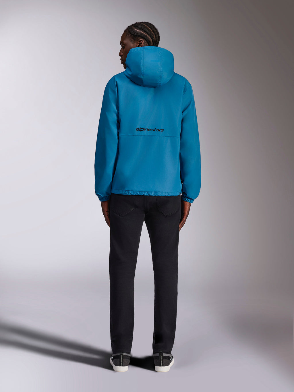Alpinestars Speeder Chromium Windbreaker-Jacke, Blauer Windbreaker, schwarzes Alpinestars-Wortlogo auf der Rückseite, Kapuzendesign, elastische Bündchen, lässige Sportbekleidung, Modell in der Rückansicht mit schwarzer Hose