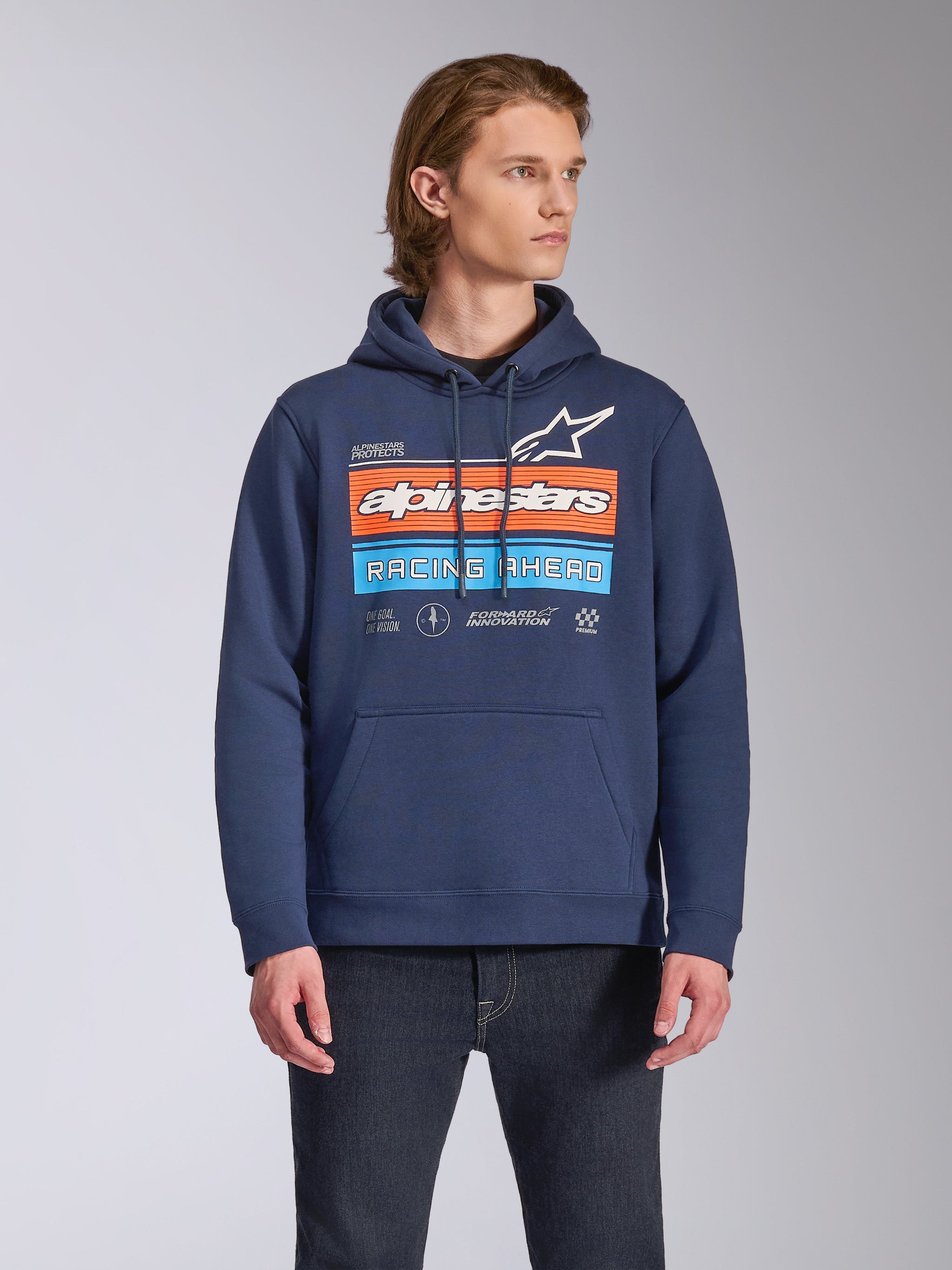 Alpinestars Harken Hoodie, lässige Streetwear, Navyblau mit „Racing Ahead“-Grafik auf der Brust in Orange und Hellblau, Fleece-Kapuzenpullover mit Kängurutasche und Kapuze mit Kordelzug, getragen von einem Model mit dunkler Jeans