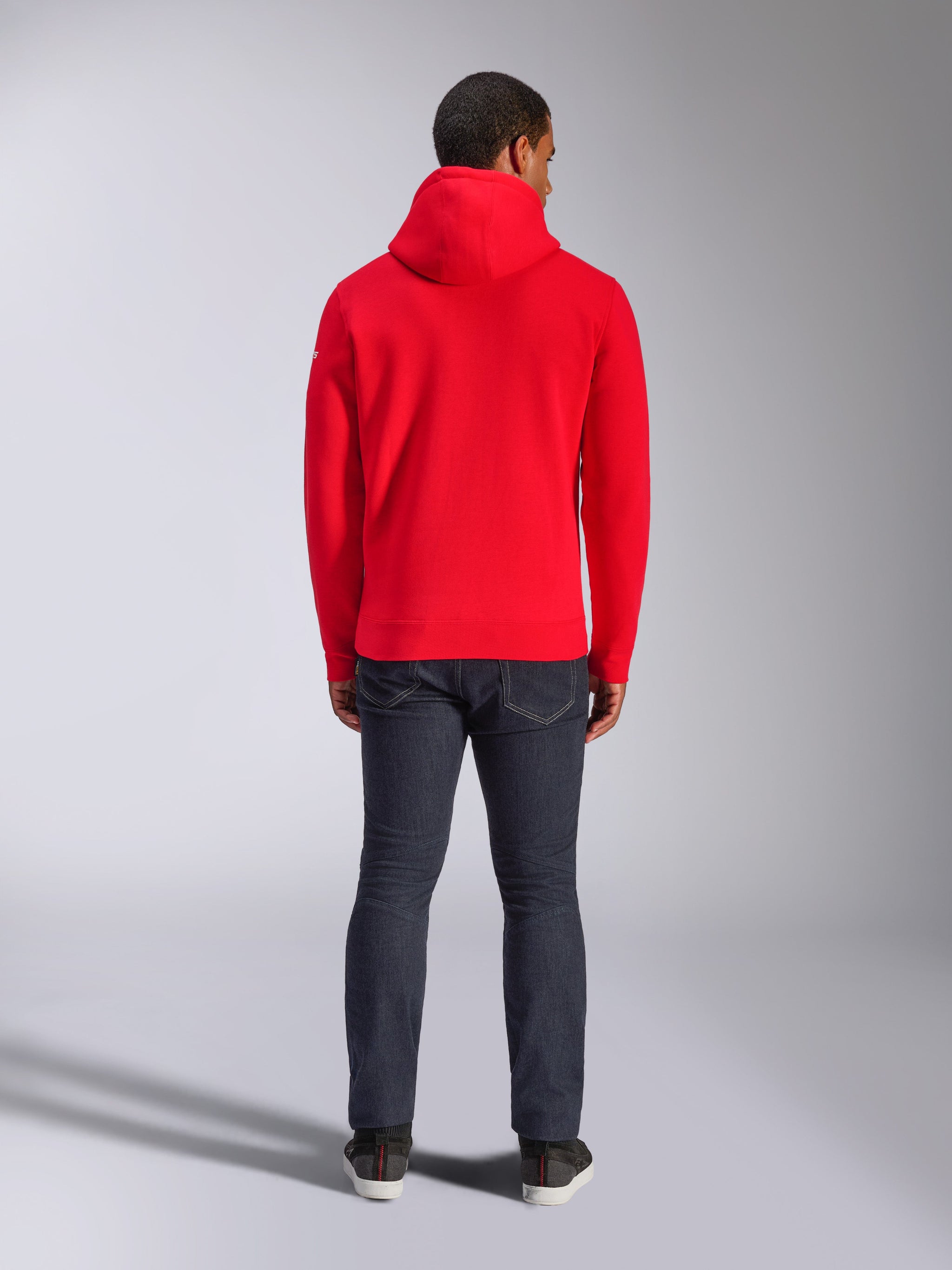 Alpinestars Frontal Hoodie, roter Pullover-Fleece-Hoodie, Rückansicht, lässiger Streetwear-Stil, getragen mit dunklen Denim-Jeans und Sneakern, mit Kapuze und geripptem Saum