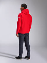 Alpinestars Frontal Hoodie, roter Pullover-Fleece-Hoodie, Rückansicht mit weißem Wortmarken-Logo auf dem Ärmel, getragen mit dunkler Jeanshose und schwarzen Schuhen, lässige Motorsport-Streetwear