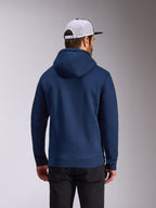 Alpinestars Frontal Hoodie, marineblauer Fleece-Pullover, Rückansicht lässiger Streetwear, getragen mit schwarzer Hose und einer weiß-schwarzen Mesh-Kappe, modernes vom Motorsport inspiriertes Design
