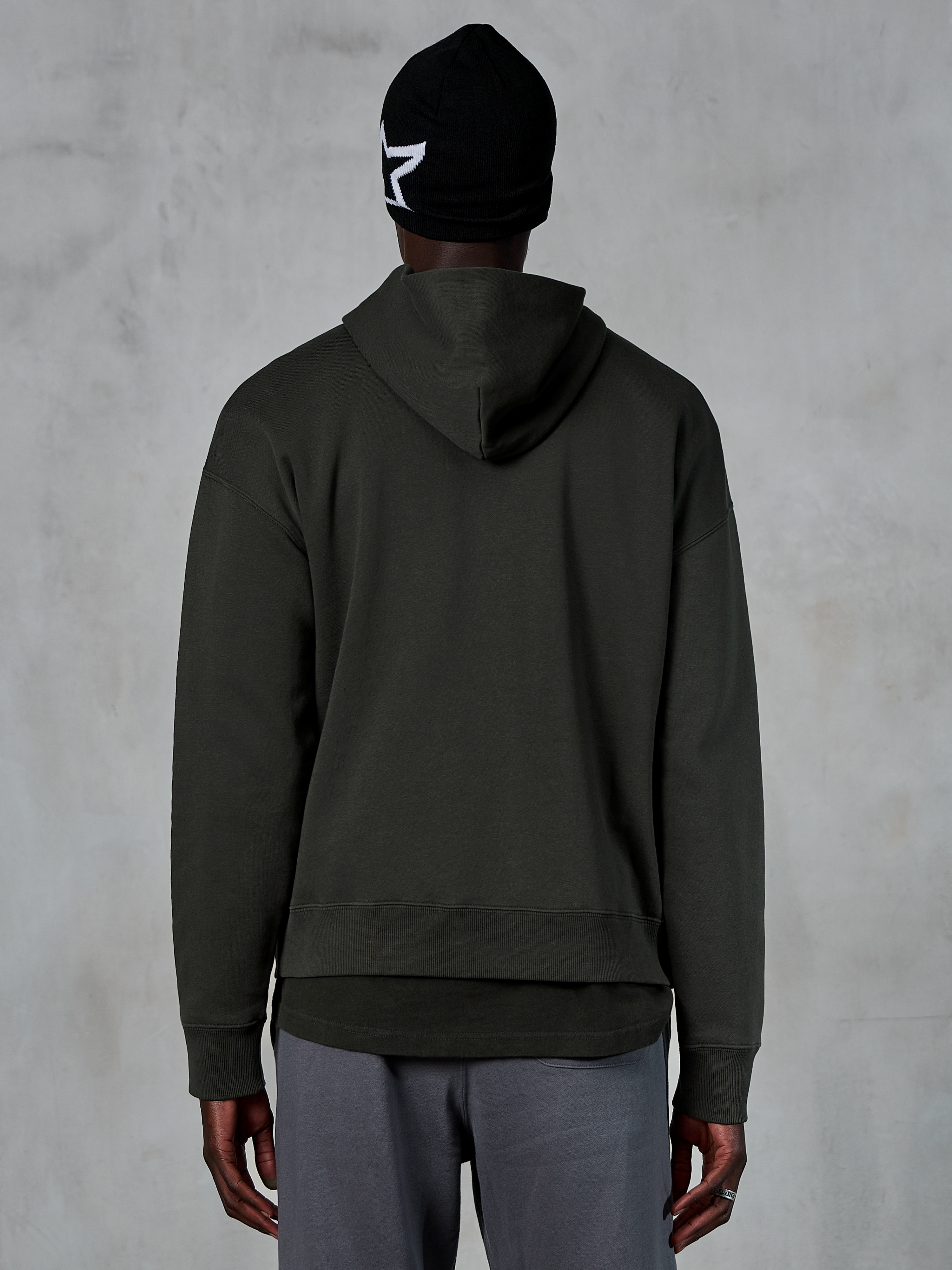 Alpinestars Essentials Ageless Hoodie, Rückansicht, Off Black, lässige Streetwear, Model mit schwarzer Beanie mit weißem Stern-Logo und grauer Hose, Premium-Fleece mit Stone-Wash-Finish