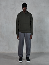 Model trägt Alpinestars Essentials Ageless Hoodie, lässige Streetwear, Off Black mit kleinem weißem Logo auf der Brust, kombiniert mit grauer Jogginghose, schwarzer Beanie und schwarzen Sneakern, minimalistisches, vom Motorsport inspiriertes Design