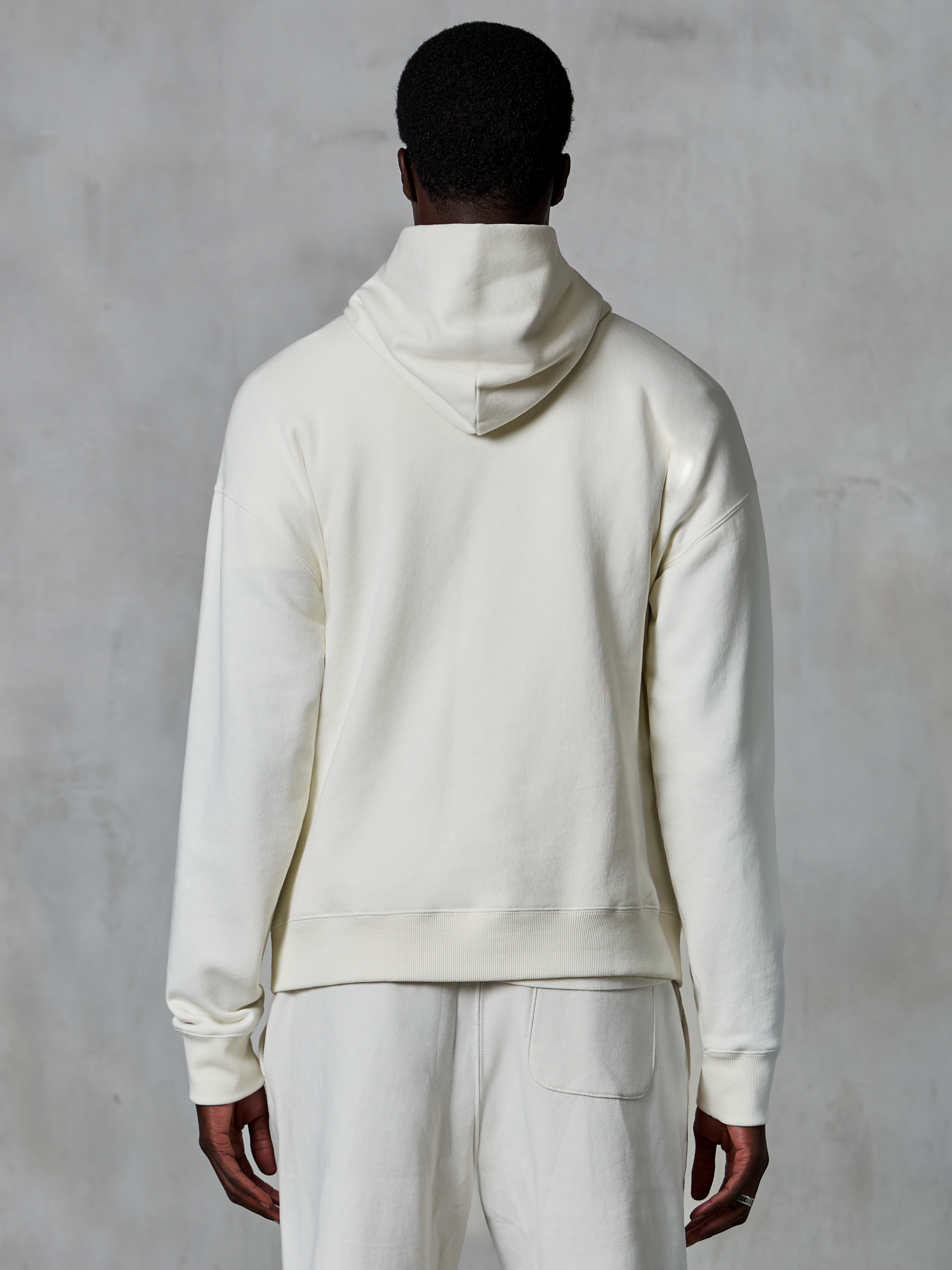 Alpinestars Essentials Ageless Kapuzenpullover, Off-White Kapuzenpullover, Rückansicht am Modell, klares minimalistisches Design, passende Freizeithose, entspannte Passform für täglichen Komfort