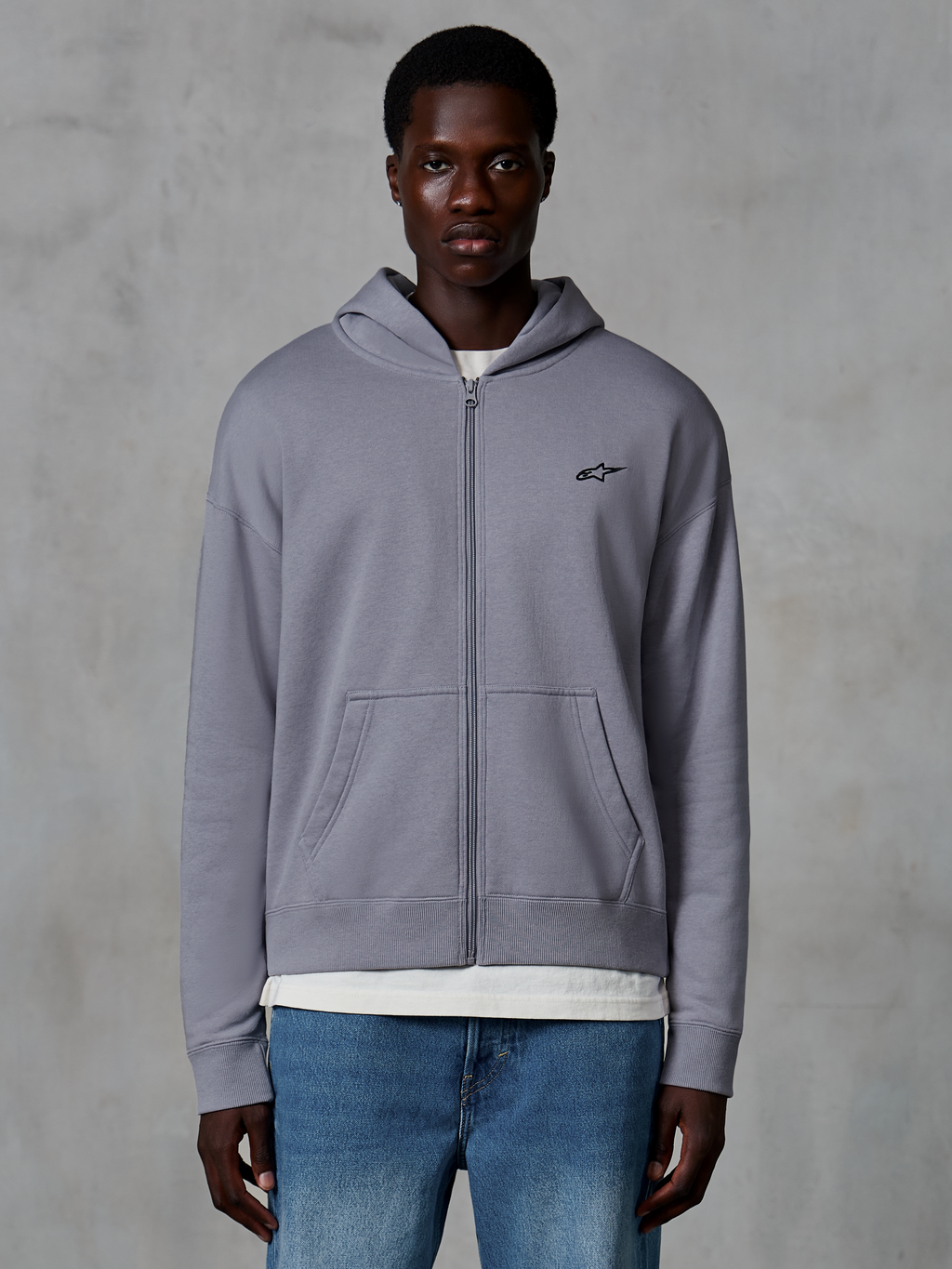 Alpinestars Essentials Ageless Zip Hoodie, Silber, lässige Streetwear von einem Model getragen, Fleece-Jacke mit durchgehendem Reißverschluss und kleinem schwarzen Astars-Logo auf der Brust, Kängurutaschen, entspannte Passform