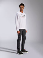Alpinestars Bettern Crew, weißes Pullover-Sweatshirt mit schwarzem Alpinestars-Logo und rotem „Racing Ahead“-Schriftzug, lässige Motorsport-Streetwear, getragen von einem Model mit dunkler Hose und schwarzen Sneakern