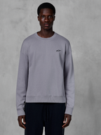 Alpinestars Essentials Ageless Crew, silbernes Rundhals-Sweatshirt von einem Model getragen, mit einem kleinen schwarzen Stern-Logo auf der Brust, entspannte Passform mit Rippbündchen und Saum, lässige Motorsport-Streetwear