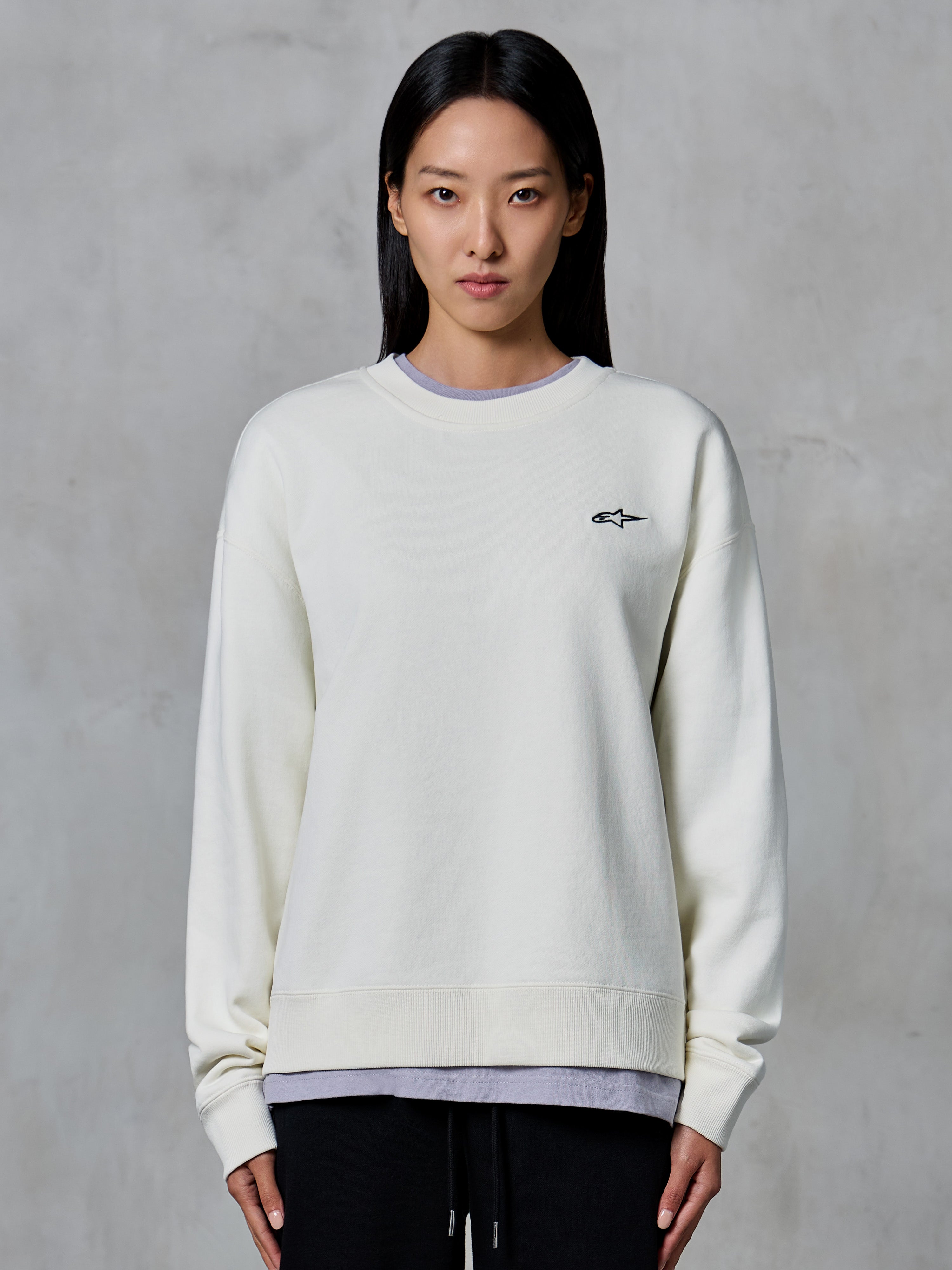 Alpinestars Essentials Ageless Crew, Rundhals-Sweatshirt, Off-White, mit einem kleinen schwarzen Alpinestars-Logo auf der Brust, lässige Lifestyle-Bekleidung, präsentiert an einer Frau