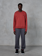 Alpinestars Essentials Ageless Crew, Brick Red crewneck sweatshirt, worn with grey sweatpants and black sneakers, featuring a small black logo on the chest, casual motorsport-inspired streetwear