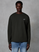 Alpinestars Essentials Ageless LS Tee, Langarm-T-Shirt, Off-Black, mit kleinem weißen Alpinestars-Logo auf der Brust, getragen von einem Modell mit blauen Jeans, lässige Streetwear aus Bio-Baumwolle