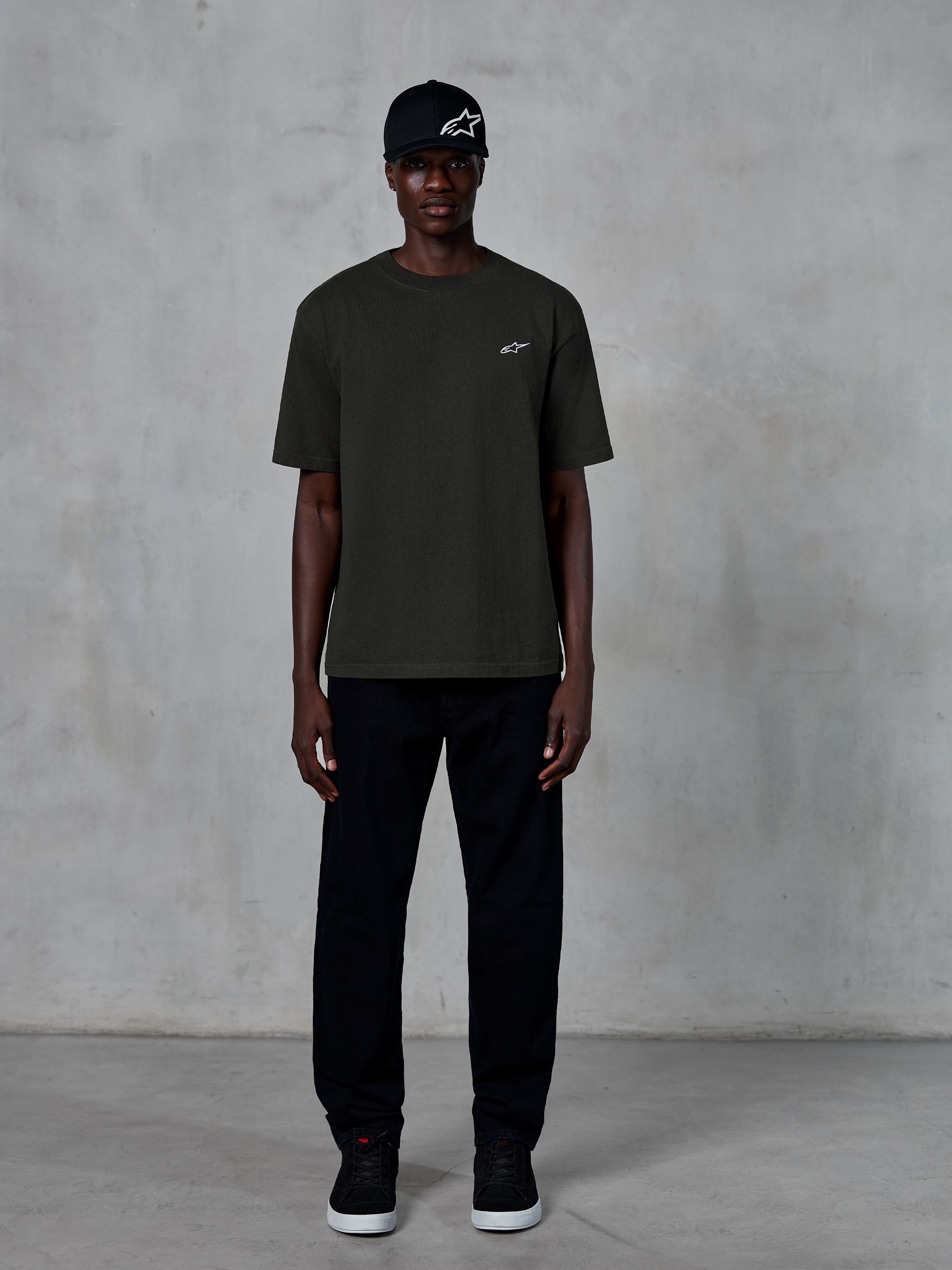 Alpinestars Essentials Ageless SS Tee, Short Sleeve T-Shirt, Off Black, featuring a small white Alpinestars logo on the chest, worn by a model with a black cap and trousers for a clean lifestyle look