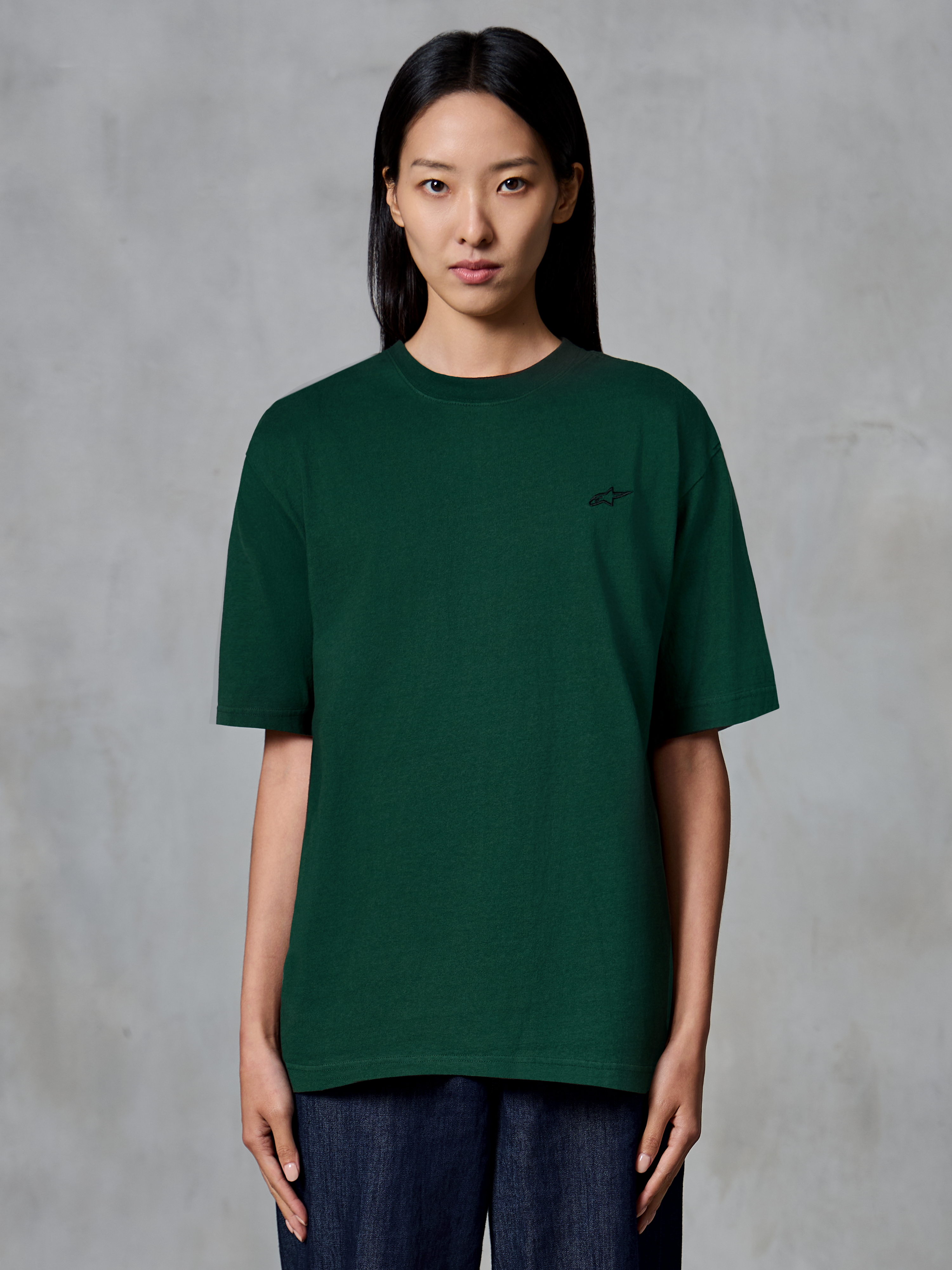 Alpinestars Essentials Ageless SS Tee, kurzärmeliges T-Shirt, Kieferngrün, von einem Modell getragen, mit kleinem schwarzen Logo auf der Brust, entspannte Passform, lässige Streetwear aus Bio-Baumwolle