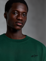 Alpinestars Essentials Ageless SS Tee, kurzärmeliges T-Shirt in Pine Green, Nahaufnahme eines Models in einem grünen Bio-Baumwoll-T-Shirt mit kleinem gesticktem Logo, lässiges Streetwear-Design