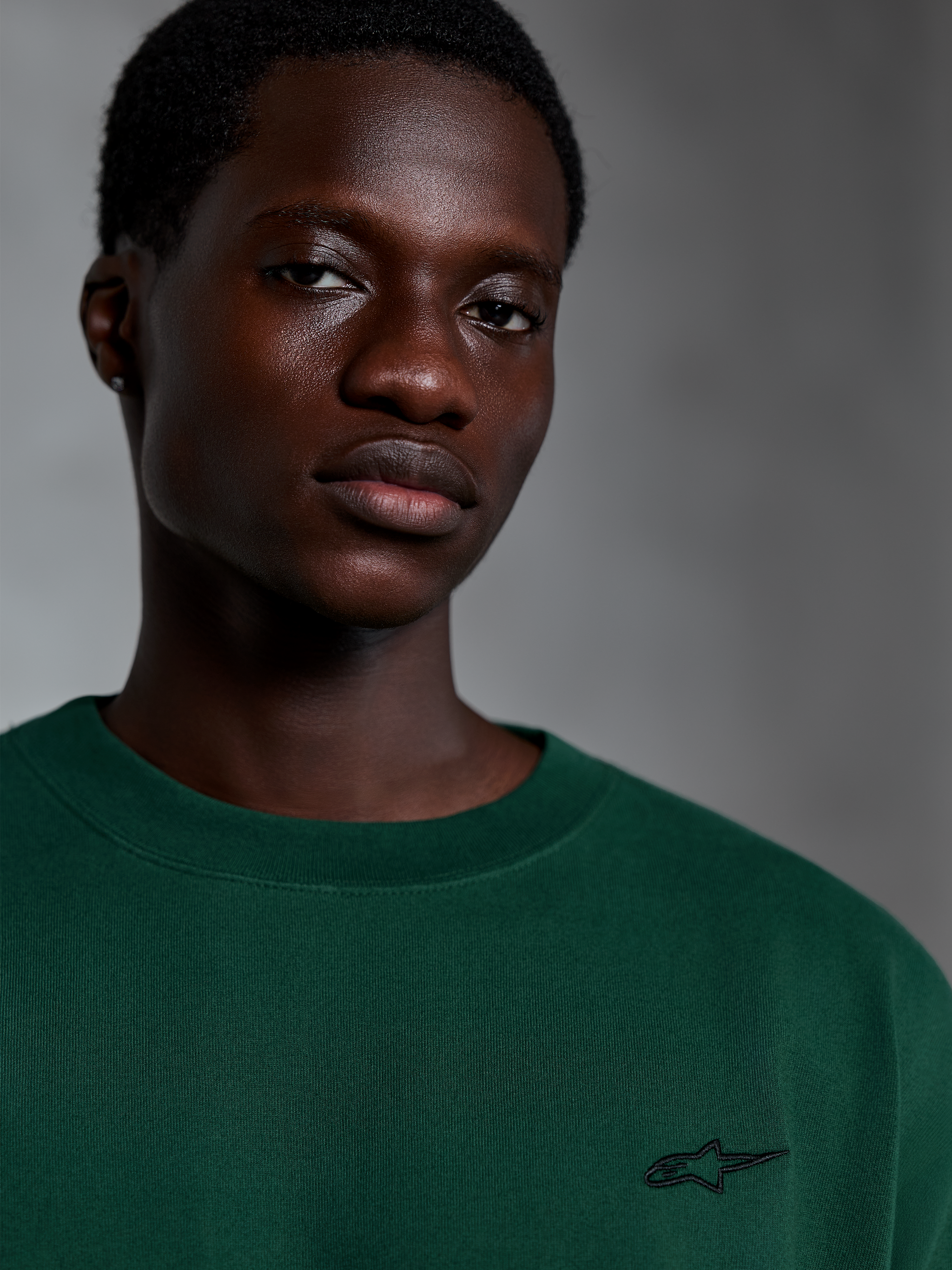 Alpinestars Essentials Ageless SS Tee, kurzärmeliges T-Shirt in Pine Green, Nahaufnahme eines Models in einem grünen Bio-Baumwoll-T-Shirt mit kleinem gesticktem Logo, lässiges Streetwear-Design