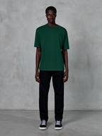 Alpinestars Essentials Ageless SS Tee, Kurzarm-T-Shirt, Pine Green, mit dezentem schwarzem Brustlogo, getragen von einem Model mit schwarzer Hose und Sneakern, lässige Lifestyle-Streetwear mit entspannter Passform