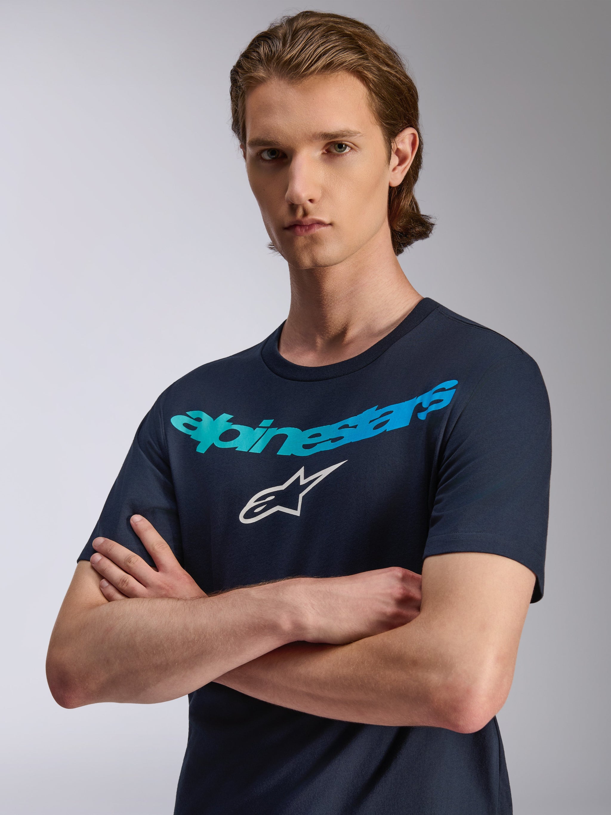 Alpinestars Collared CSF T-Shirt, Kurzarm-T-Shirt, Dunkelblau, Alpinestars-Schriftzug mit türkisem Farbverlauf und weißem Stern-Logo, Modell mit verschränkten Armen, lässige Performance-Sportbekleidung