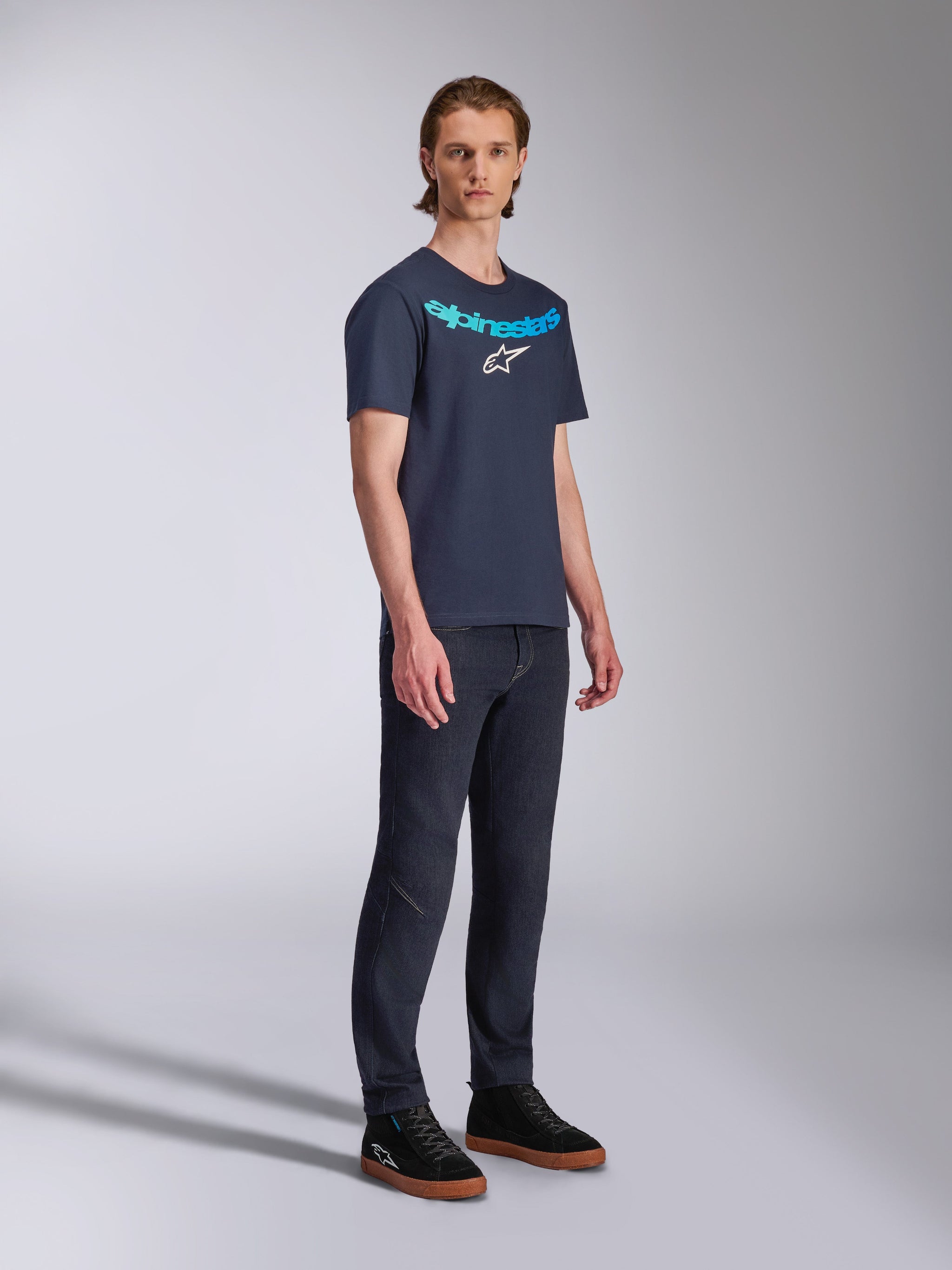 Alpinestars Collared CSF Tee, kurzärmeliges T-Shirt, Navyblau, hellblauer Alpinestars-Schriftzug und weißes Stern-Logo auf der Brust, getragen von einem Model mit dunkler Jeanshose und schwarzen Sneakern, lässiger Sportbekleidungsstil