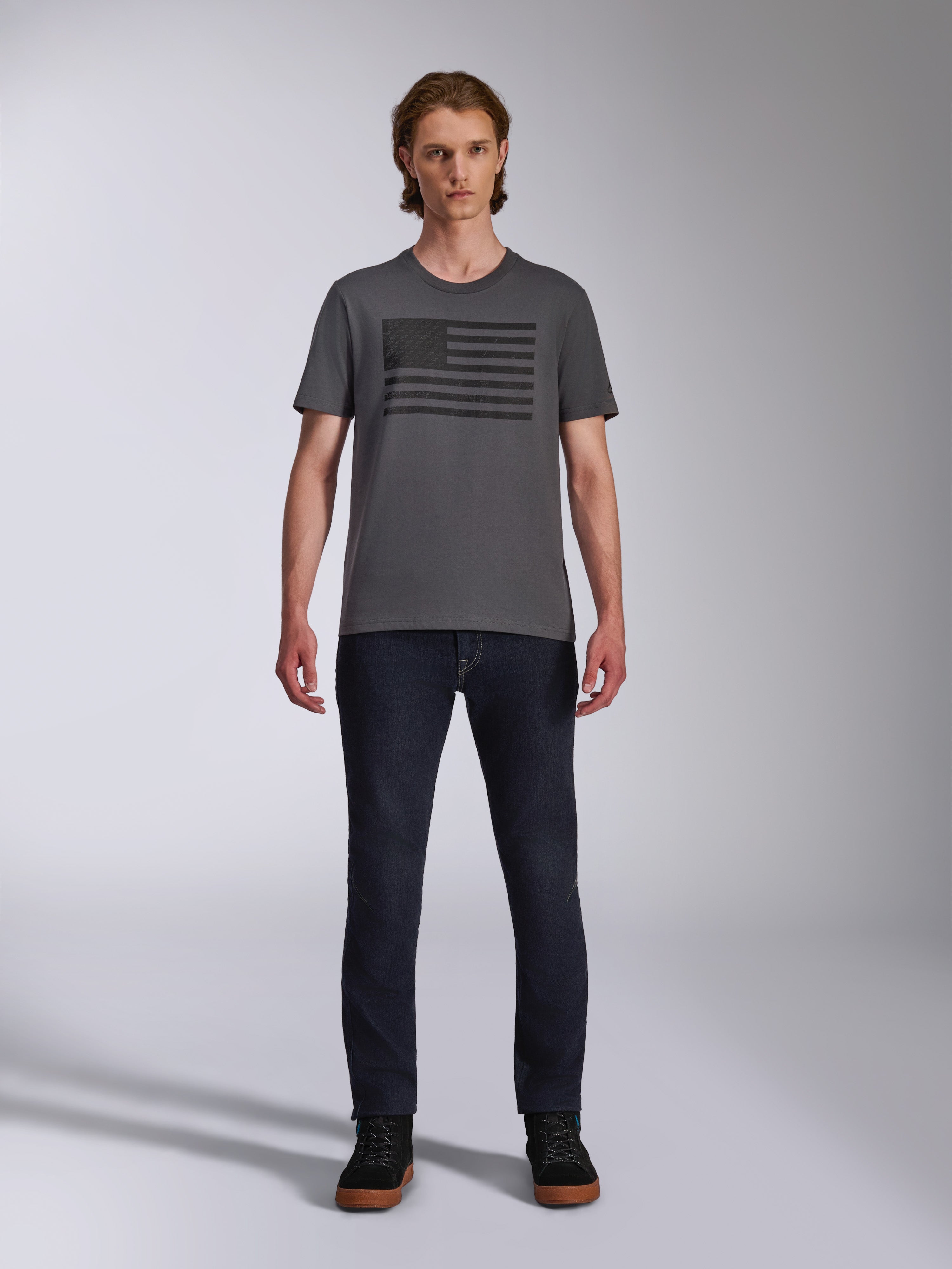 Alpinestars Waving CSF Tee, Kurzarm-T-Shirt, Anthrazitgrau, schwarze Blaze 2.0 Grafik im Flaggen-Stil, lässige Motorsport-Streetwear, getragen mit dunklen Denim-Jeans