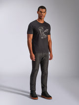 Alpinestars Tech Boot CSF Tee, Short Sleeve T-Shirt, Black, featuring a white tech boot graphic and logo on the chest, worn by a model with dark denim pants and black sneakers, casual motorsport-inspired streetwear