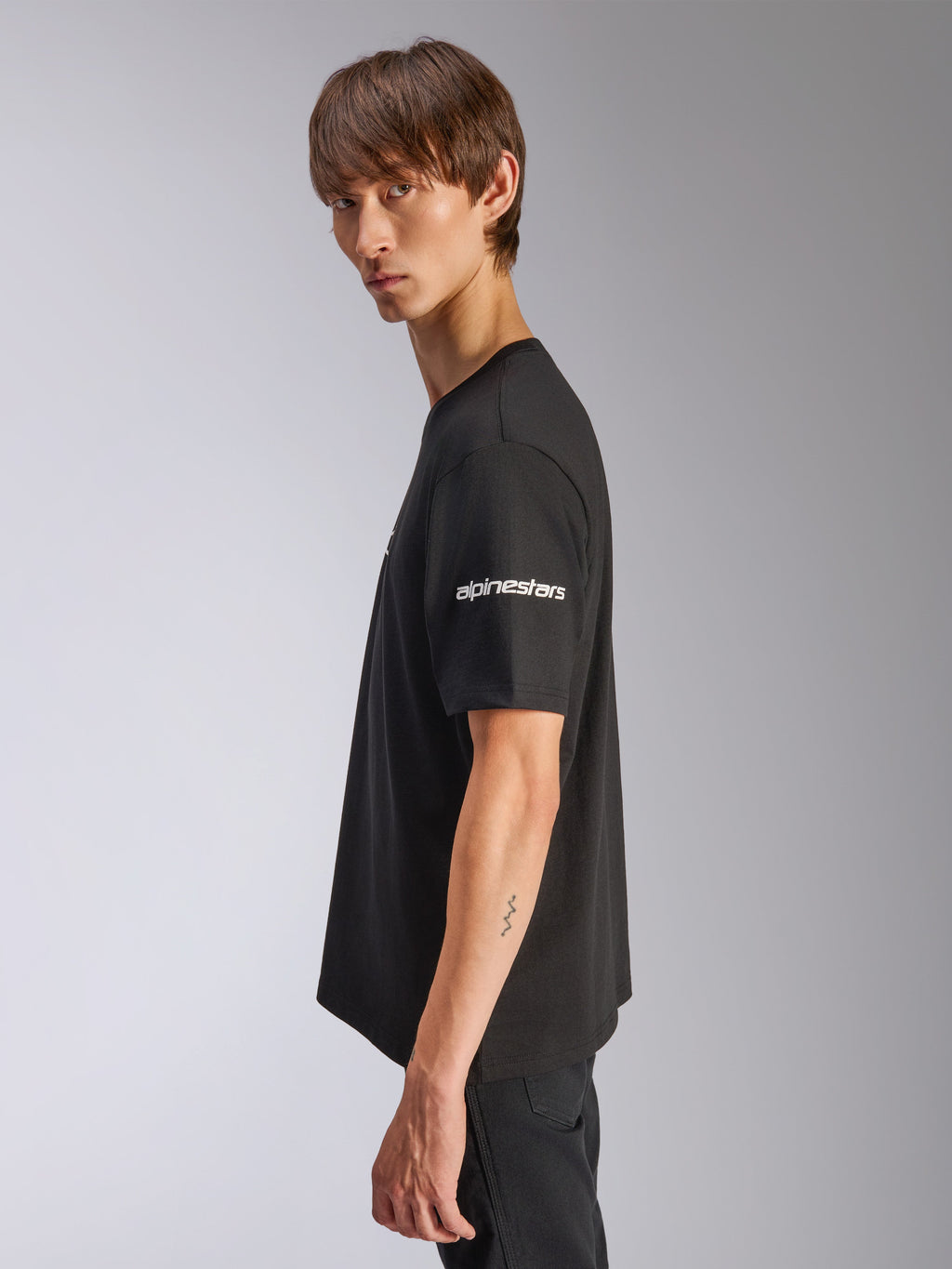Alpinestars Frontal CSF Tee, Kurzarm-T-Shirt, Schwarz, weißes Alpinestars-Logo auf dem Ärmel, von einem Modell in der Profilansicht getragen, lässige Motorsport-Performance-Streetwear