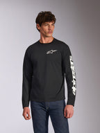 Alpinestars Trackside CSF Langarmshirt, Schwarz, weißes Alpinestars-Logo auf der Brust und Branding am Ärmel, getragen von einem Model mit blauen Jeans, lässige Motorsport-Streetwear