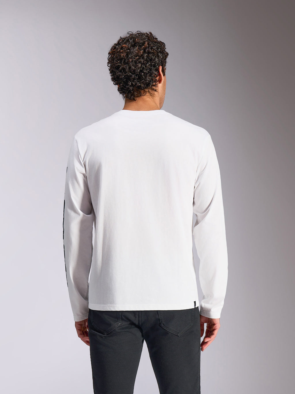 Alpinestars Trackside CSF Langarm-T-Shirt, Weiß, Rückansicht am Modell, kombiniert mit schwarzer Hose, reiner weißer Stoff mit langen Ärmeln, lässige, vom Motorsport inspirierte Streetwear