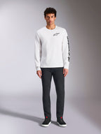 Alpinestars Trackside CSF Langarmshirt, Weiß mit schwarzem Branding, kleines Logo auf der Brust und vertikaler Schriftzug am Ärmel, getragen von einem Model mit dunkler Hose und schwarzen Sneakern, lässige, vom Motorsport inspirierte Streetwear