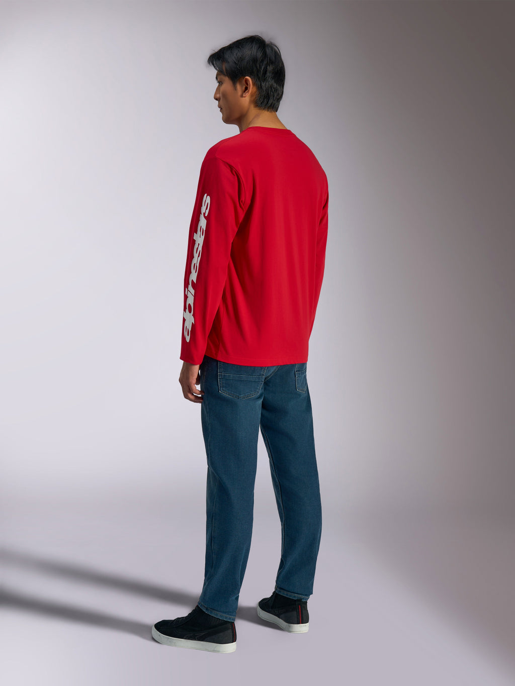 Alpinestars Trackside CSF Tee, Langarmshirt, Rot, mit weißem vertikalem Alpinestars-Logo auf dem Ärmel, getragen von einem Model mit blauen Jeans und schwarzen Sneakern, lässige Motorsport-inspirierte Streetwear