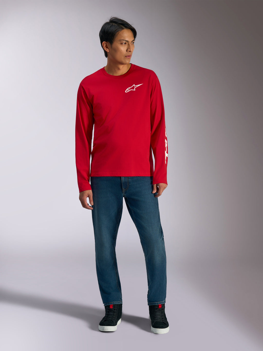 Alpinestars Trackside CSF Tee, Langarmshirt, Rot mit weißem Alpinestars-Logo, Lifestyle-Aufnahme getragen mit blauen Jeans und schwarzen Sneakern, lässige, vom Motorsport inspirierte Sportbekleidung