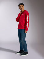 Alpinestars Trackside CSF Langarmshirt, Rot mit weißem Alpinestars-Branding auf Brust und Ärmel, getragen von einem Model mit blauen Jeans und schwarzen Sneakern, lässige, vom Motorsport inspirierte Streetwear