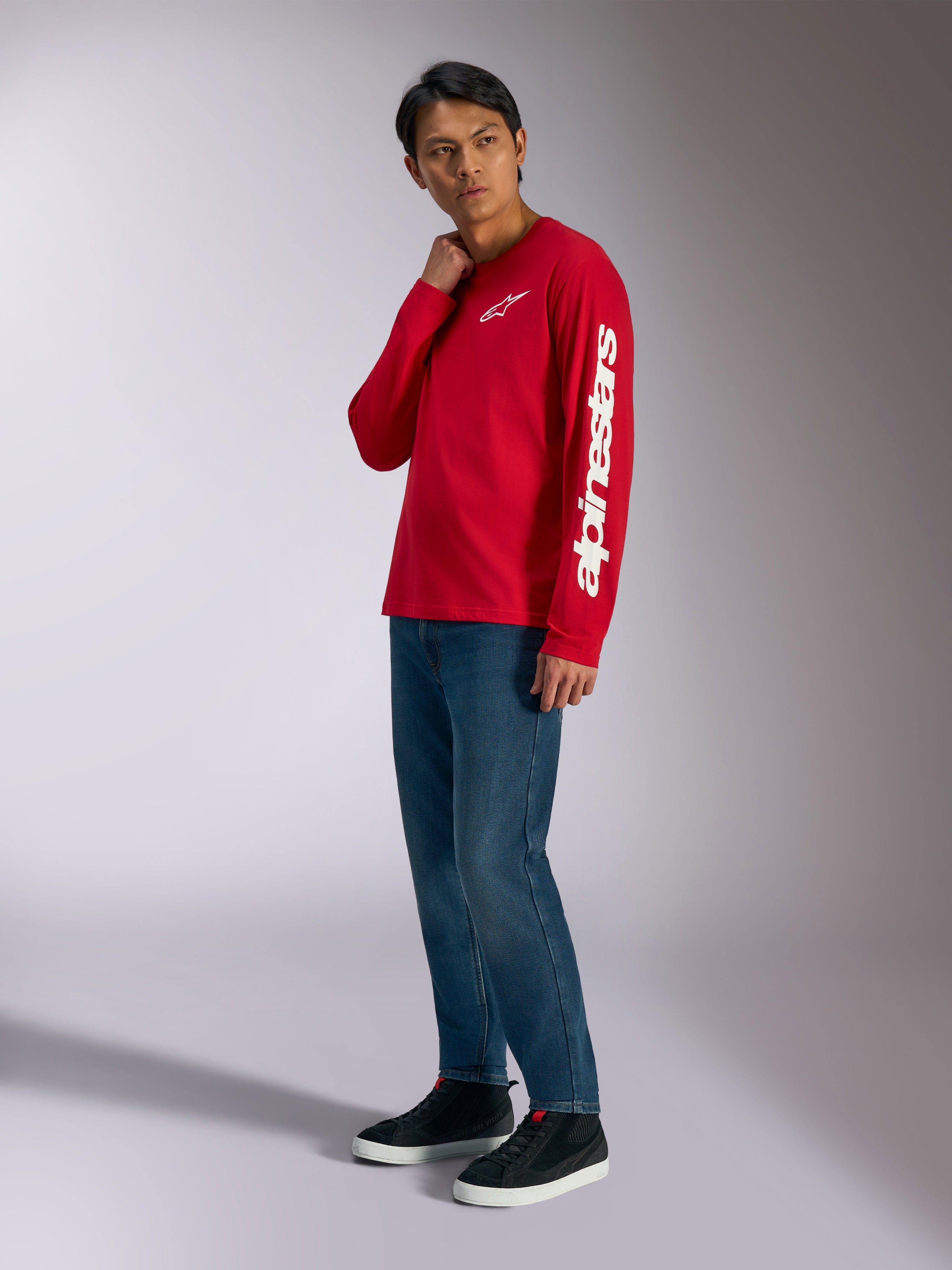 Alpinestars Trackside CSF Langarmshirt, Rot mit weißem Alpinestars-Branding auf Brust und Ärmel, getragen von einem Model mit blauen Jeans und schwarzen Sneakern, lässige, vom Motorsport inspirierte Streetwear