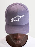 Alpinestars Ageless Snapback Kappe, Freizeitkappe in Staublila und Weiß, mit gebogenem Schirm, strukturierter Krone und aufgesticktem 3D-Astars-Logo auf der Vorderseite, getragen von einem Model