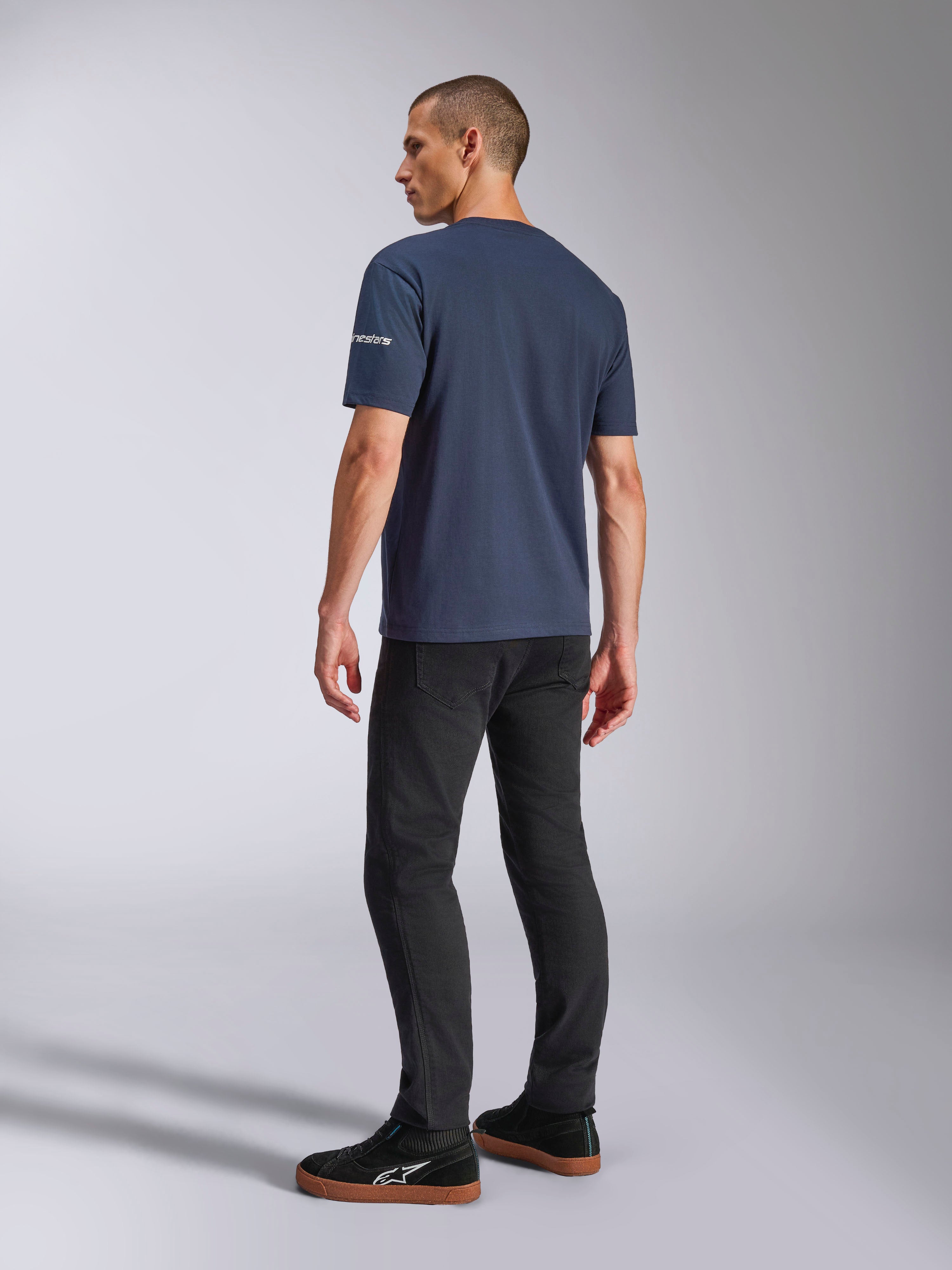 Alpinestars Frontal CSF Tee, Kurzarm-T-Shirt, Marineblau, Rückansicht am Modell mit Ärmel-Logo, getragen mit schwarzer Hose und Sneakern, lässige, vom Motorsport inspirierte Streetwear