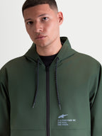 Alpinestars Speeder Resolve Windbreaker Jacket, lightweight hooded sportswear windbreaker in Pine Green, featuring an adjustable hood with speckled drawstrings and signature Alpinestars branding on the chest, worn by a male model.
