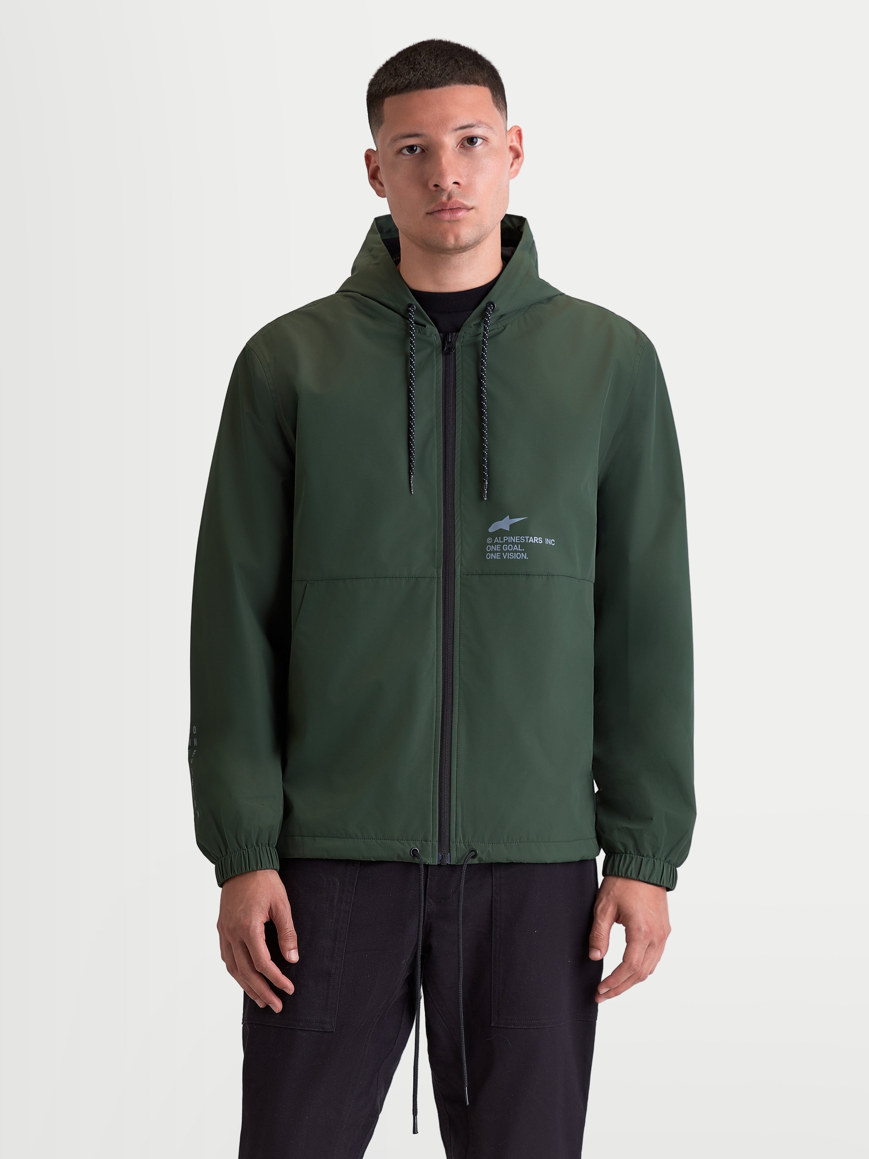 Alpinestars Speeder Resolve Windbreaker Jacket, Lightweight Hooded Sportswear on Model, Pine Green, Featuring Reverse-Coil Zipper, Adjustable Hood, and Signature Chest Branding with One Goal One Vision Motto