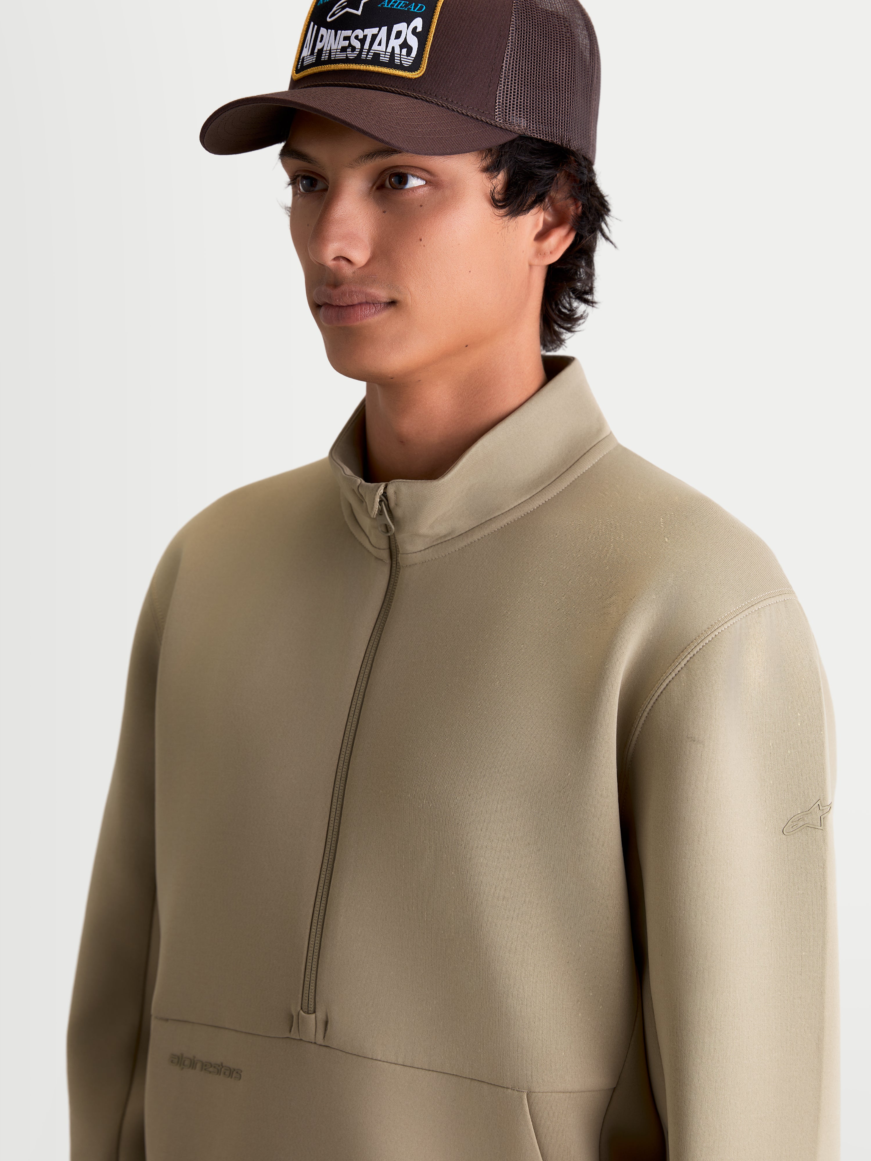Alpinestars Apera Half-Zip Sweatshirt, beiger Sportswear-Pullover mit Halbreißverschluss und Kängurutasche, Motorsport-inspiriertes Oberteil aus Tri-Blend-Fleece, am Model gezeigt.