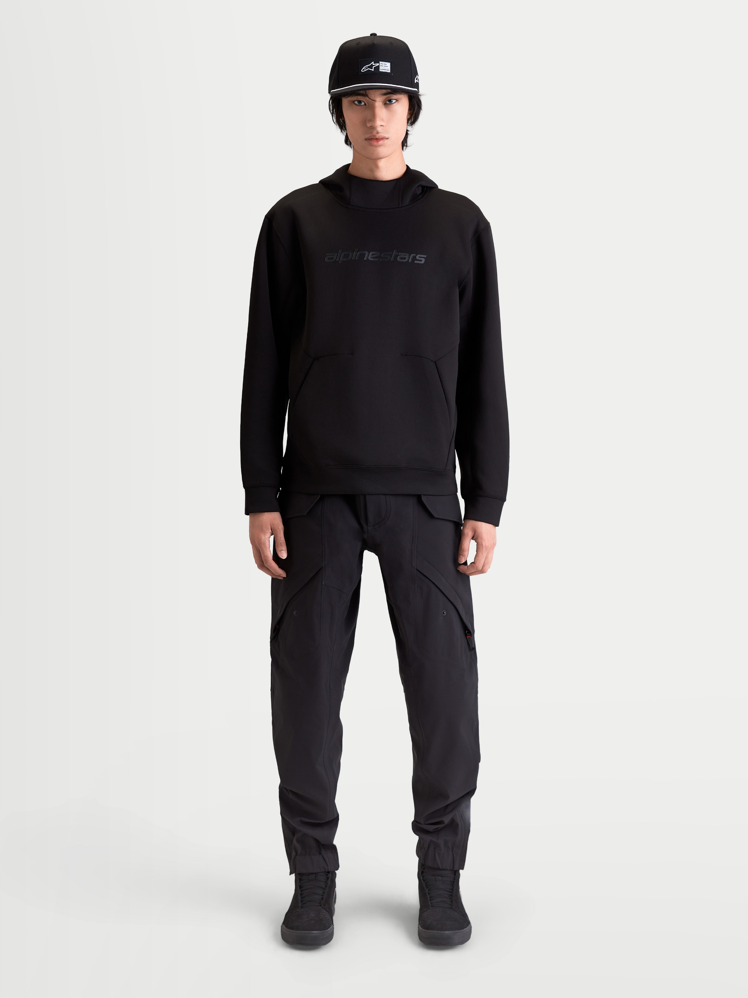 Alpinestars Datrix Hoodie, Herren Sportswear-Kapuzenpullover, Schwarz, mit tonalem HD-Branding, Tri-Blend-Doppelfleece und Tasche mit Abnäherdetail, am Modell präsentiert für einen motorsport-inspirierten Alltagsstil.