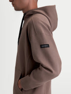 Alpinestars Camino Textured Oversized Hoodie, Sportswear Kapuzenpullover in Braun, Seitenansicht am Model mit strukturiertem Strick-Twill-Fleece und gewebtem Alpinestars-Ärmellabel, lässige Oversized-Passform.