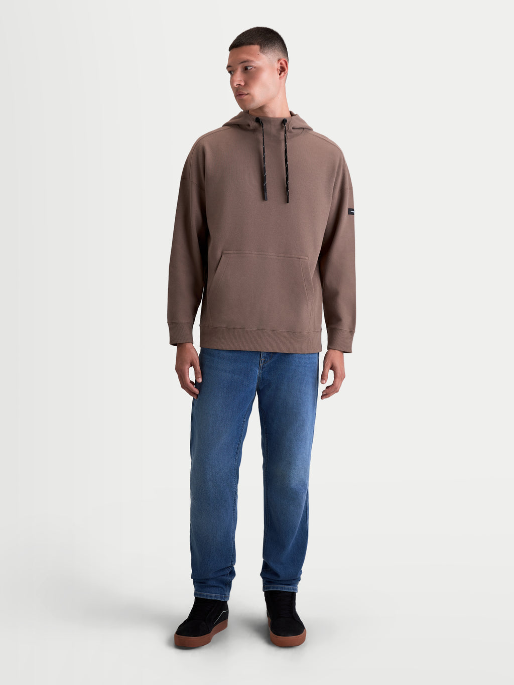 Alpinestars Camino Textured Oversized Hoodie, Herren-Sportswear-Pullover, Braun, strukturierter Stricktwill-Fleece, hoher Kragen mit Kordelzug und Kängurutasche in entspannter Silhouette, am Modell getragen.