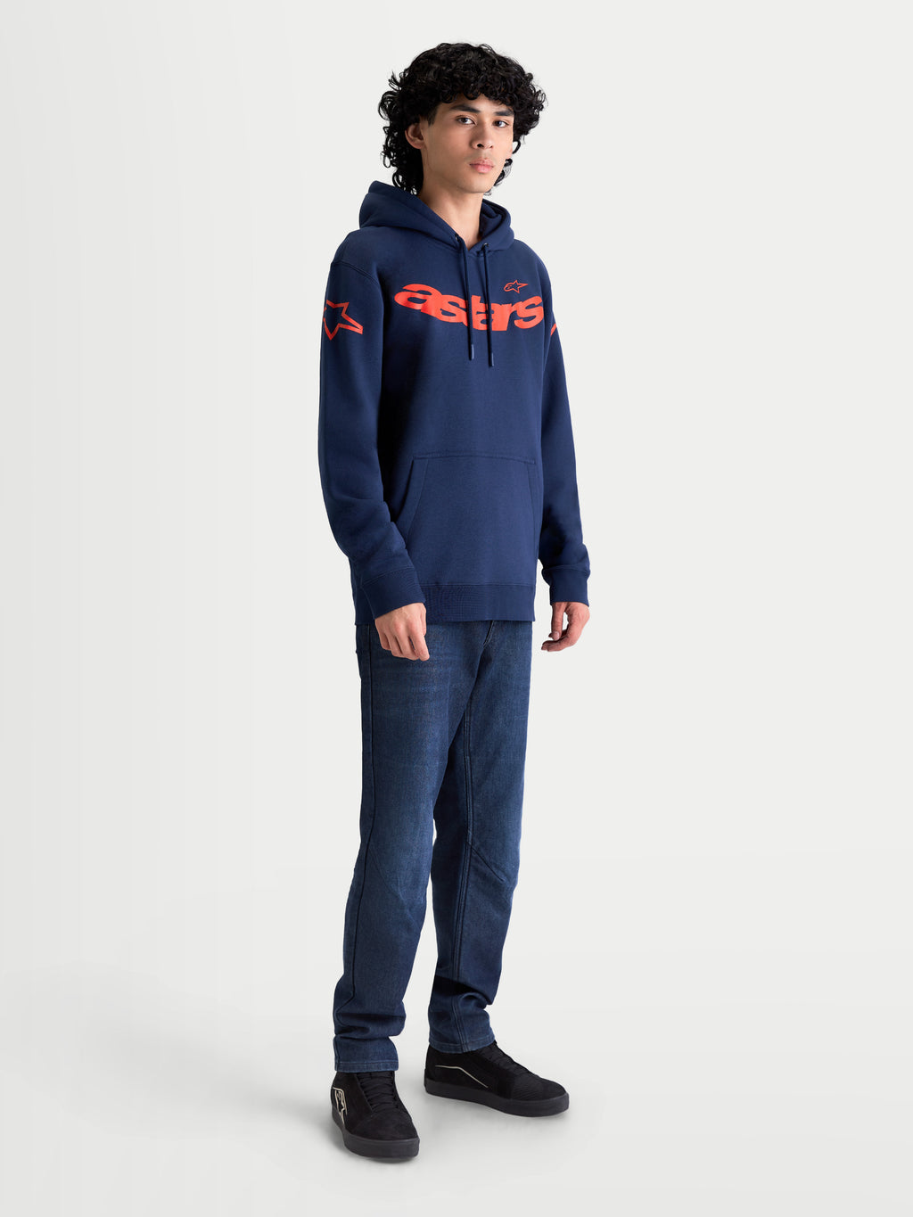 Alpinestars Velocifier Hoodie, Herren-Sportswear-Kapuzenpullover in Marineblau und Orange, mit markantem Astars-Schriftzug auf der Brust und Schulterlogos, am Model präsentiert für einen lässigen, vom Motorsport inspirierten Look abseits des Bikes.