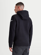 Alpinestars Race Wordmark Hoodie, Sportswear-Kapuzenpullover, Rückansicht am Modell, Schwarz und Weiß, mit weißem Ageless-Stern-Logo auf dem linken Ärmel, Kapuze mit Eigenmaterial-Futter und Rippbündchen, hochwertige Baumwoll- und Recycling-Polyester-Mischung.