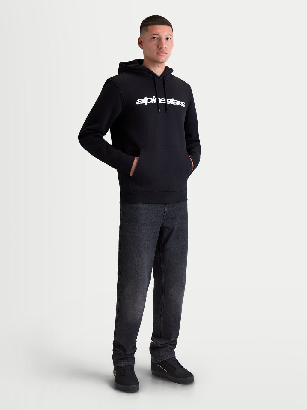 Alpinestars Race Wordmark Hoodie, Herren Kapuzenpullover aus Fleece, Schwarz und Weiß, mit markantem weißem Brustlogo, Kapuze mit Kordelzug und Kängurutasche vorne. Hergestellt aus einer Baumwollmischung mit recyceltem Polyester für den Alltag, am Modell präsentiert.