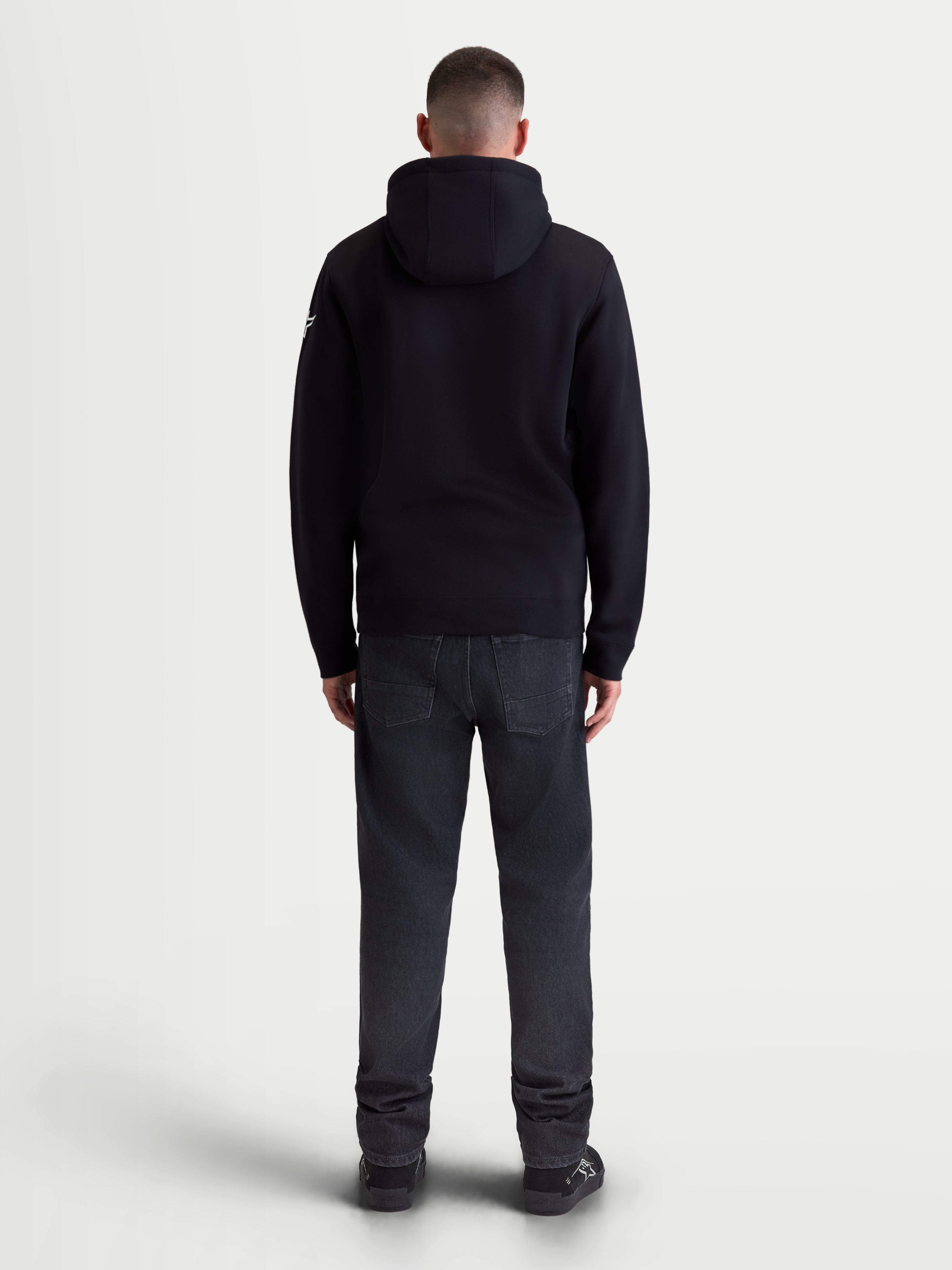 Alpinestars Race Wordmark Hoodie, Herren-Sportswear-Kapuzenpullover aus Fleece, Schwarz und Weiß, Rückansicht eines Models im schwarzen Kapuzenpullover, mit gefütterter Kapuze und bequemer Baumwollmischung für den täglichen Motorsport-Lifestyle.