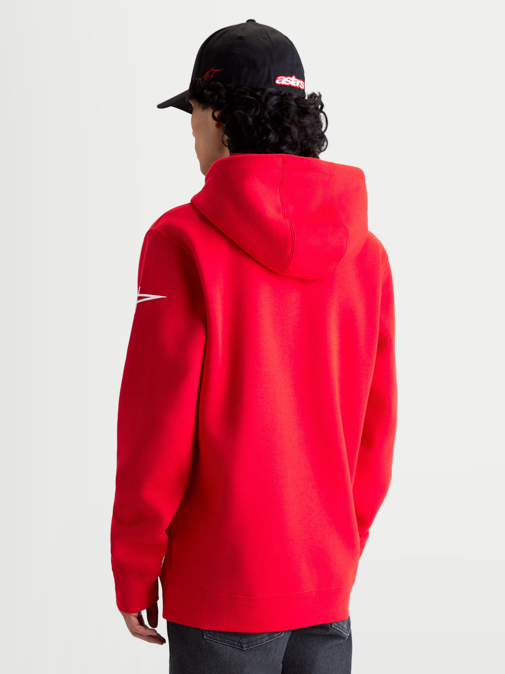 Alpinestars Race Wordmark Hoodie, roter und weißer Sportswear-Kapuzenpullover aus Fleece, Rückansicht am Modell mit Kapuze und weißem Ageless-Ärmellogo, hochwertige Baumwoll- und Recycling-Polyester-Mischung für einen lässigen Motorsport-Lifestyle.